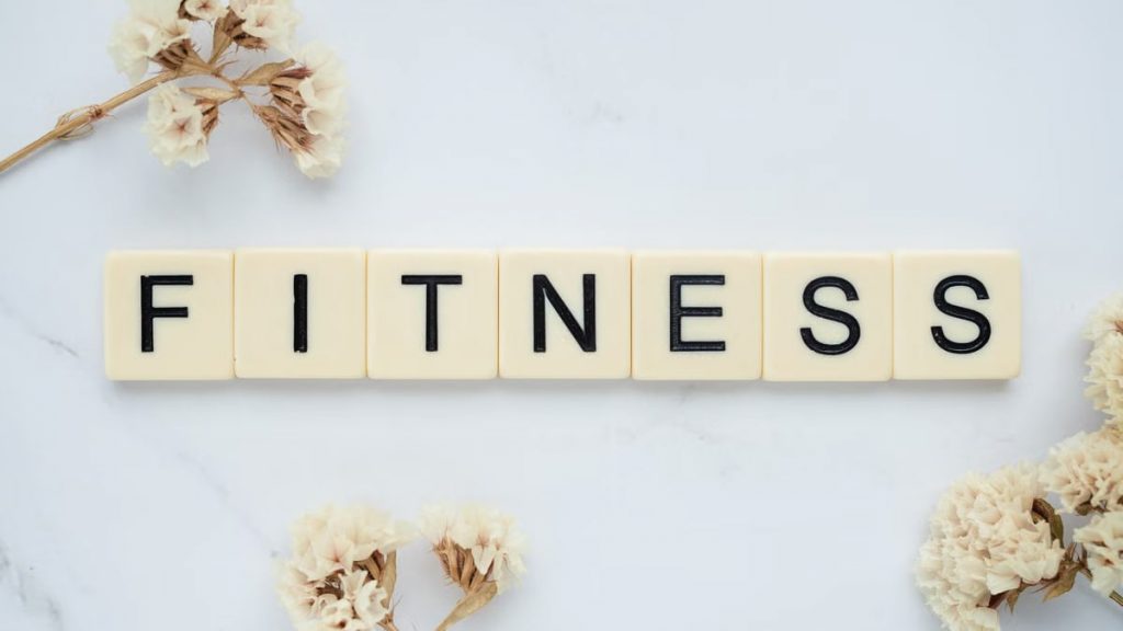 Close-up of scrabble tiles spelling 'FITNESS' on a marble surface with white flowers.