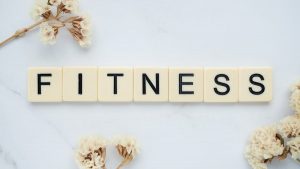 Close-up of scrabble tiles spelling 'FITNESS' on a marble surface with white flowers.